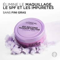 Le pot de baume demaquillant violet est pose sur une texture vaporeuse et violette rappelant un nuage de produit. Le texte en haut a gauche indique : « ELIMINE LE MAQUILLAGE, LE SPF ET LES IMPURETES SANS FINI GRAS ».