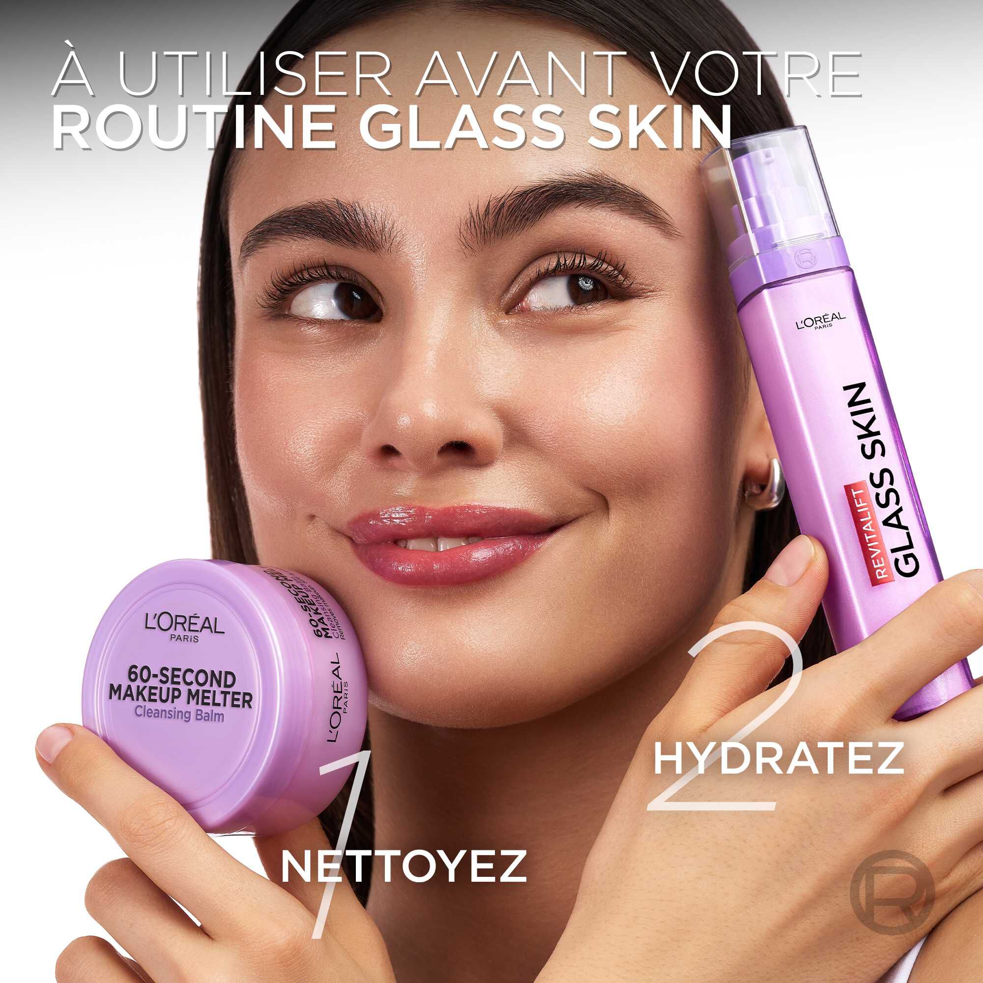 Une mannequin sourit en presentant la routine de soin en deux etapes. Elle tient le baume demaquillant violet dans sa main droite, marque du chiffre « 1 NETTOYEZ », et un flacon pulverisateur violet "GLASS SKIN" dans son autre main, marque du chiffre « 2 HYDRATEZ ». Le texte principal est : « A UTILISER AVANT VOTRE ROUTINE GLASS SKIN ».