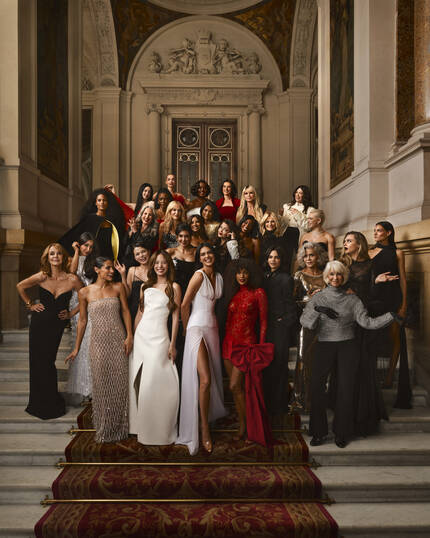 Une image marquante de la campagne L'Oreal Paris presente Kendall Jenner. Elle est elegamment vetue d'une robe noire avec une cape spectaculaire et fluide. L'arriere-plan est une representation sophistiquee en noir et blanc d'un grand batiment parisien historique. Le texte 'LE DEFILE' est affiche en lettres rouges en haut de l'image, avec le logo 'L'OREAL PARIS' dans le coin superieur gauche. En dessous de 'LE DEFILE', la devise inspirante 'LIBERTE. EGALITE. SORORITE. VOUS LE VALEZ BIEN.' est ecrite en rouge. Dans le coin inferieur droit, le logo 'PARIS FASHION WEEK' est visible.