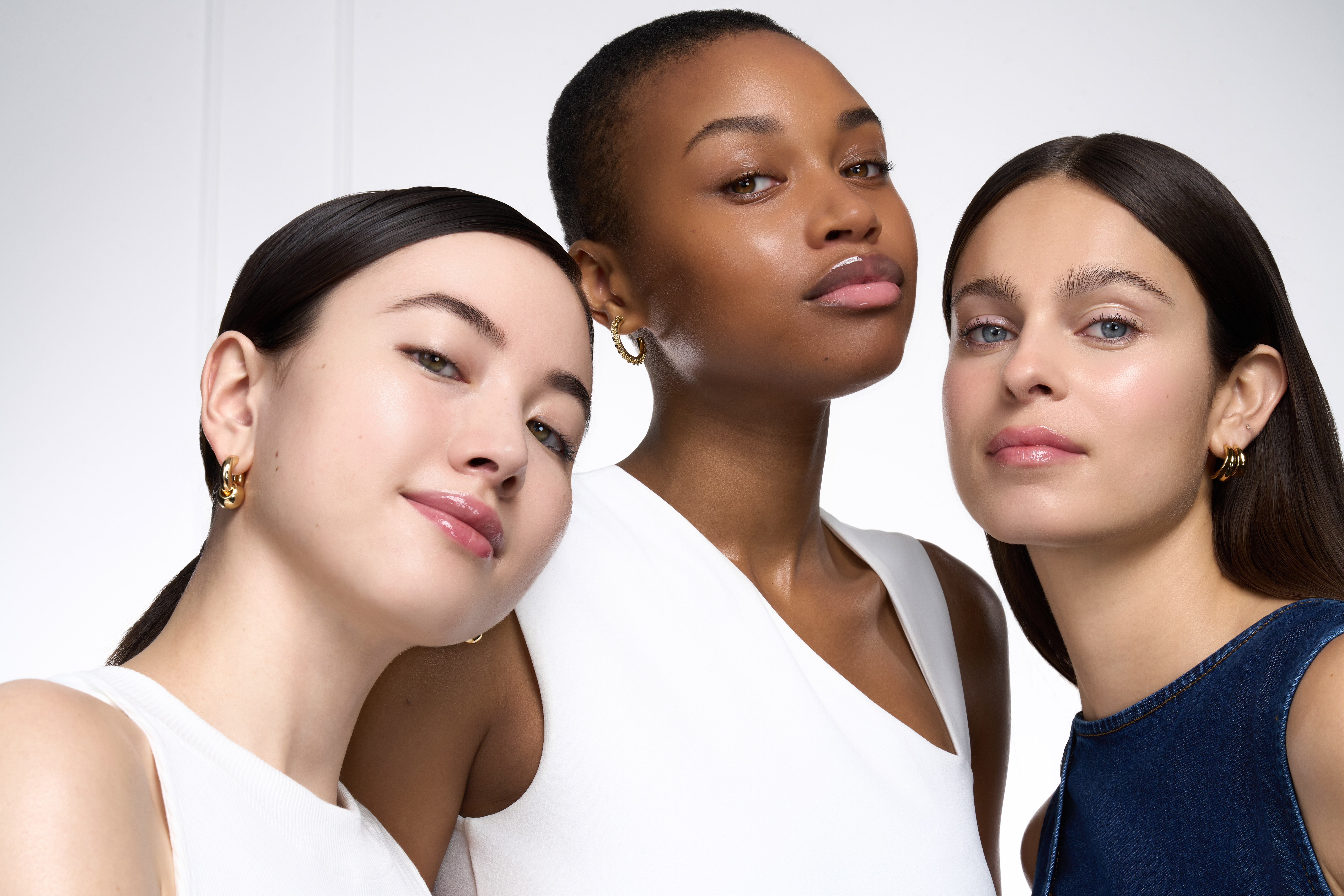 Trois femmes aux carnations variees, peaux lumineuses et cheveux fonces, posent avec confiance.